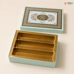 A decorative rectangular gift box set from Bakeyy, featuring a light aqua exterior with an ornate floral and geometric pattern on the lid, and a gold-foil lined interior with four compartments, shown open on a warm beige background.