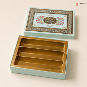 A decorative rectangular gift box set from Bakeyy, featuring a light aqua exterior with an ornate floral and geometric pattern on the lid, and a gold-foil lined interior with four compartments, shown open on a warm beige background.