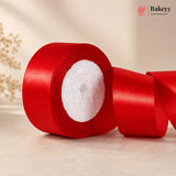 Red satin ribbon roll on a light wooden surface with 'Bakeyy' branding.