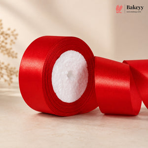 Red satin ribbon roll on a light wooden surface with 'Bakeyy' branding.