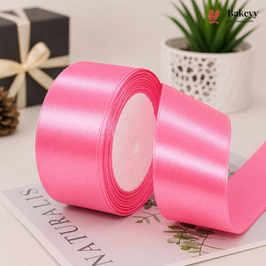 Roll of pink satin ribbon on a magazine with a plant and gift box in the background