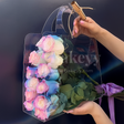 Transparent bag with colorful roses and green leaves held by a hand against a dark background.