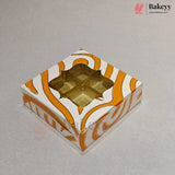 A square bakery box with a white and orange wavy pattern, featuring a clear window that reveals four gold foil cupcake liners inside, set on a light gray background.