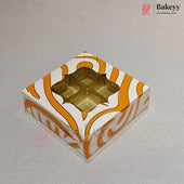 A square bakery box with a white and orange wavy pattern, featuring a clear window that reveals four gold foil cupcake liners inside, set on a light gray background.