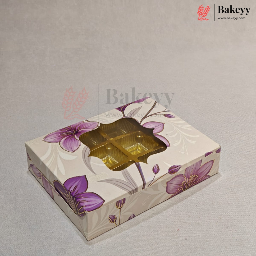 A rectangular bakery gift box with a floral pattern in purple and beige, featuring a clear window on top that reveals four golden-brown individually wrapped pastries inside. The box is photographed on a neutral light gray background with a 'Bakeyy' watermark logo in the upper right corner.