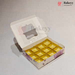 An open white bakery box with a clear window on the lid and yellow-gold individual tray compartments inside, shown on a light gray background. The box has purple floral illustrations on the sides, and a Bakeyy logo watermark is visible.