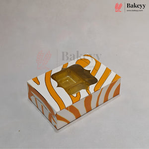 A small rectangular bakery box with a zebra-like orange and white pattern, featuring a clear plastic window on top that reveals a golden-brown tray of pastries inside. The box is photographed on a plain light gray background with faint Bakeyy watermarks.