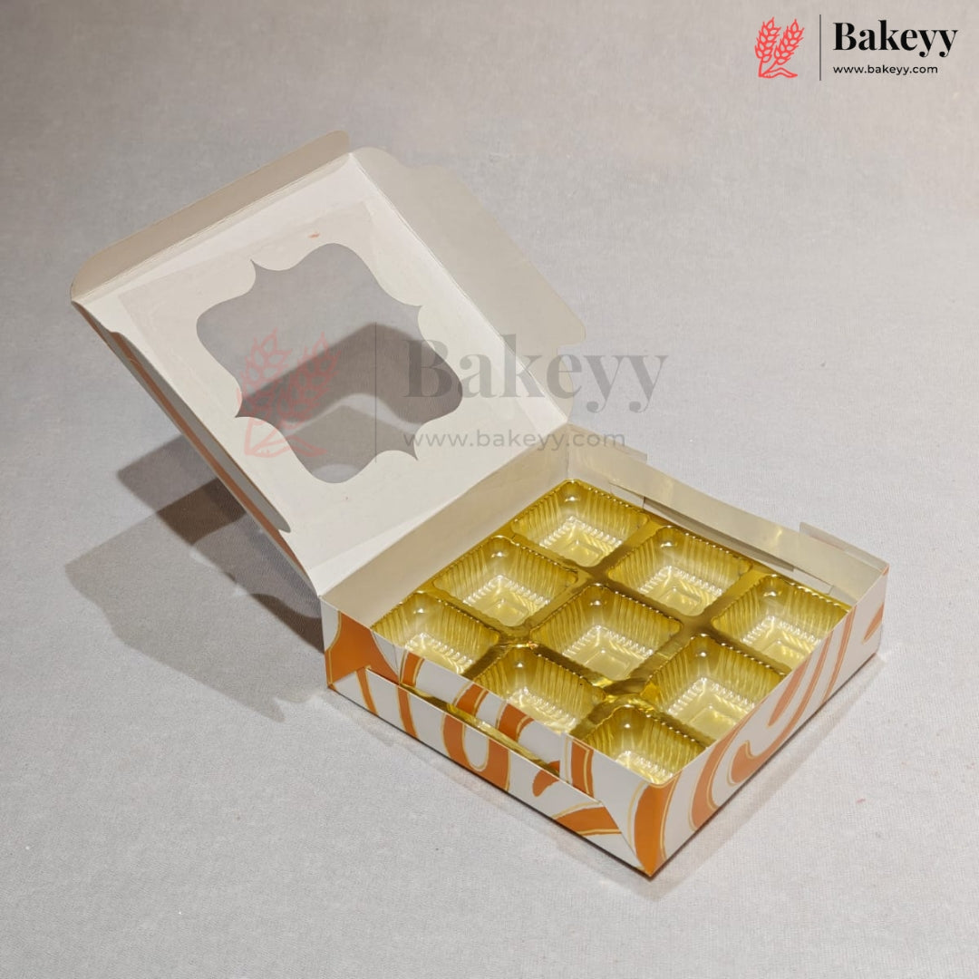 An open bakery box with a hinged lid, featuring a clear window on the lid and nine gold foil compartments inside. The box has orange and white decorative patterns on the base.
