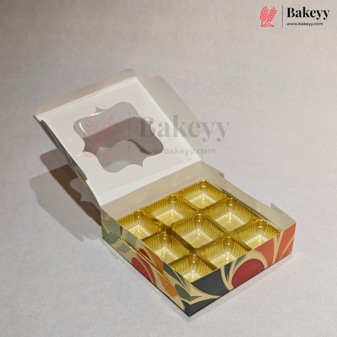 An open bakery box with a hinged lid, featuring a clear window on the lid and nine gold-colored cup-like compartments on the bottom. The box has a decorative pattern on the sides with red, orange, green, and black shapes.