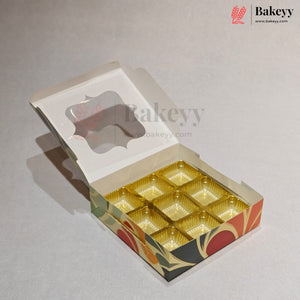 An open bakery box with a hinged lid, featuring a clear window on the lid and nine gold-colored cup-like compartments on the bottom. The box has a decorative pattern on the sides with red, orange, green, and black shapes.