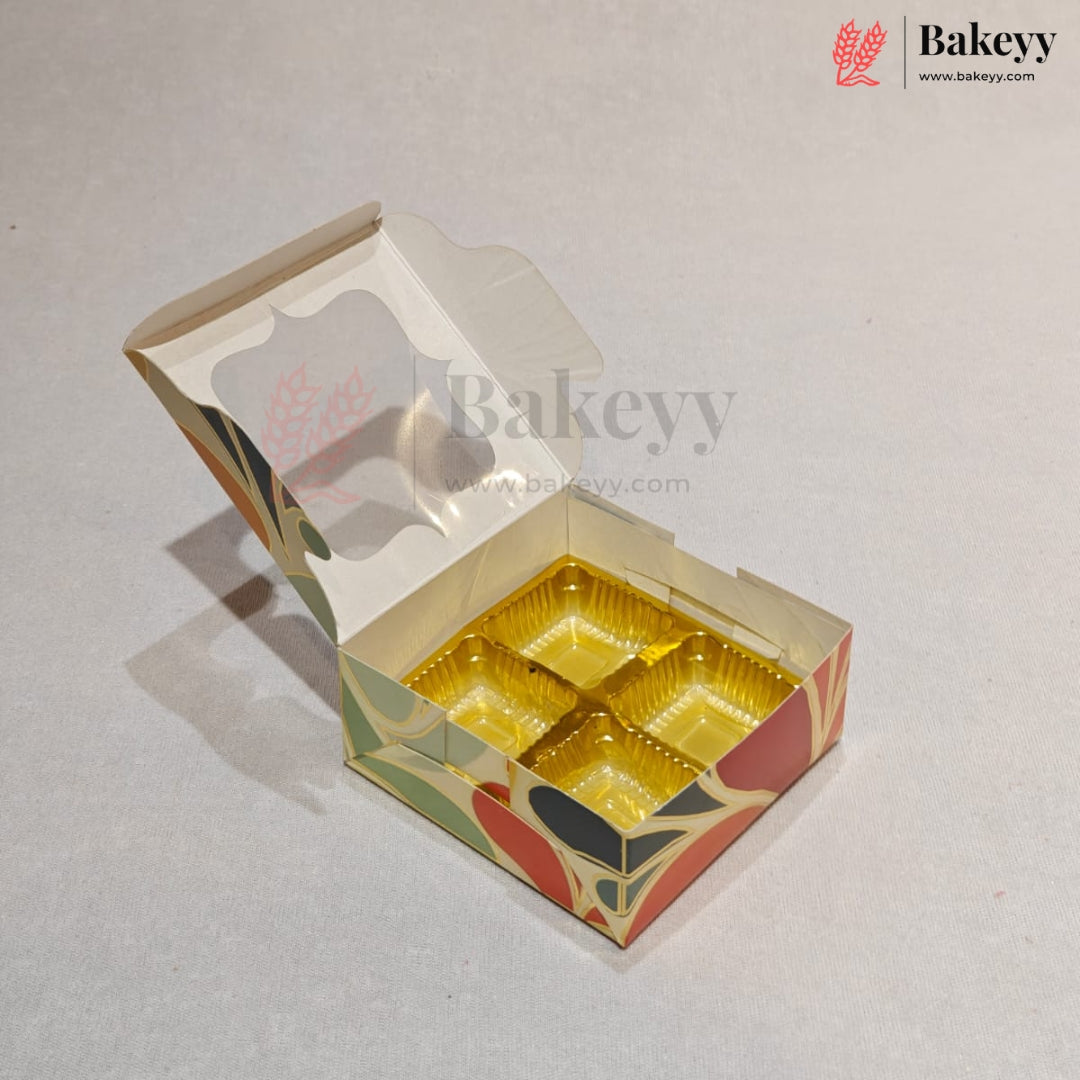 An open custom cardboard bakery box with four compartments lined with shiny gold foil, featuring a cream base with red, green, and black floral patterns. The Bakeyy logo is visible in the top right corner.