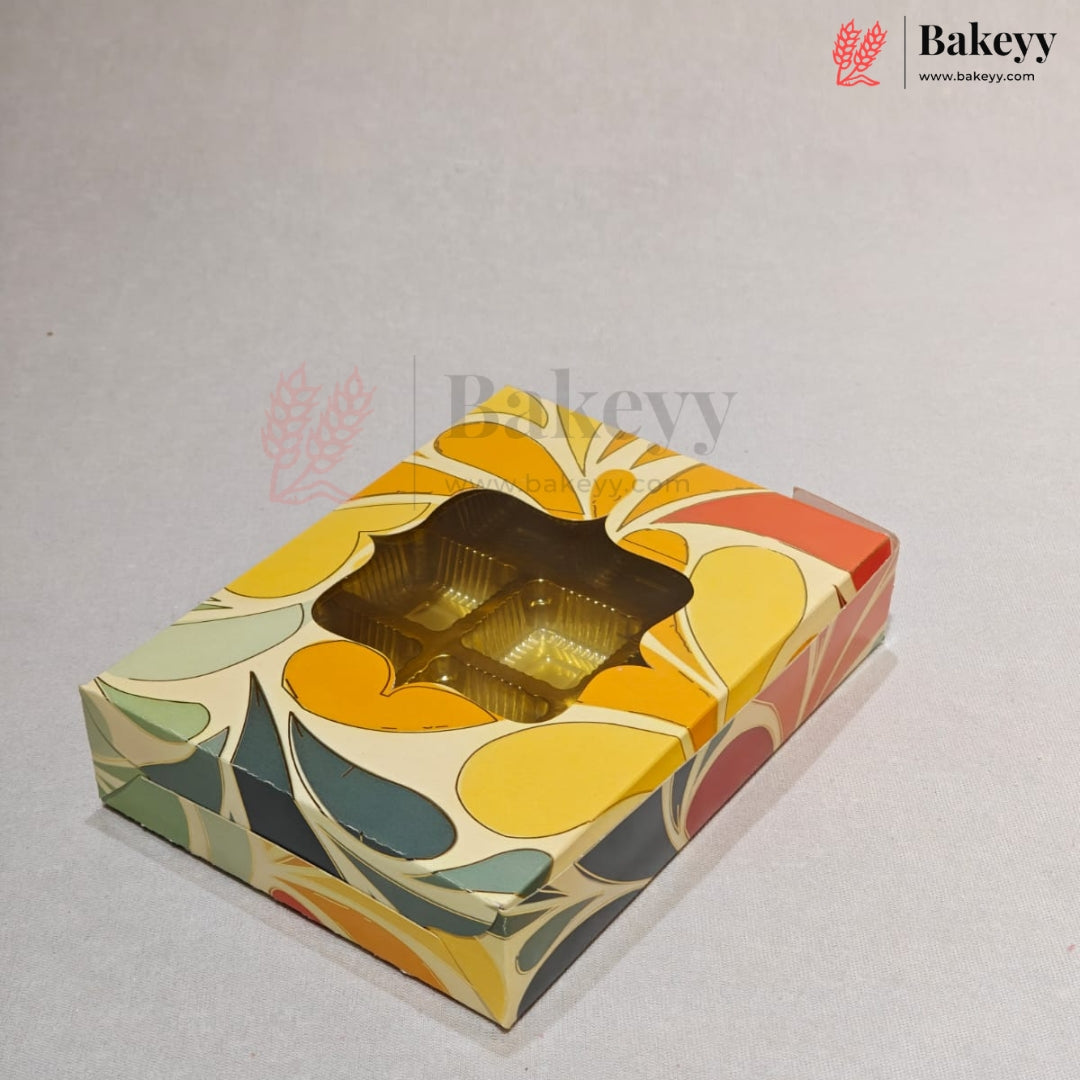 A square bakery box with a colorful retro floral pattern in yellow, orange, green, and red on a cream background, featuring a clear window showing a gold-colored tray inside. The Bakeyy logo is visible in the top right corner.