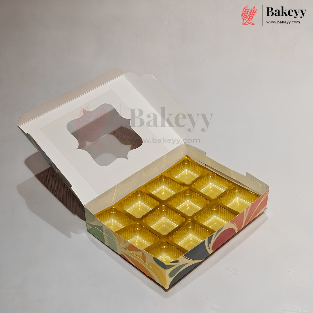 An open bakery box with a hinged lid and a clear window, showing 12 individual gold-colored cupcake or muffin liners arranged inside. The box has a white outer flap and a colorful printed base with green, orange, and red patterns.