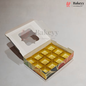 An open bakery box with a hinged lid and a clear window, showing 12 individual gold-colored cupcake or muffin liners arranged inside. The box has a white outer flap and a colorful printed base with green, orange, and red patterns.