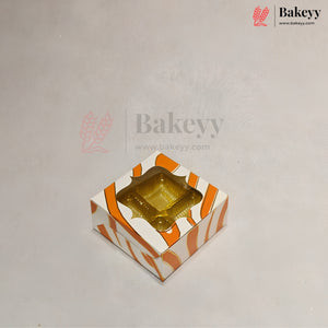 A square bakery box with a clear plastic window on top, decorated with orange and white diagonal stripes, shown on a light gray background with Bakeyy branding.