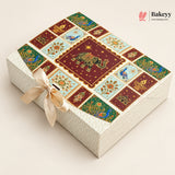 A rectangular decorative gift box with a cream-colored textured exterior and lid featuring a colorful patchwork design of maroon, green, and light blue panels with peacocks, elephants, and floral motifs. A cream satin ribbon is tied in a bow on the front.