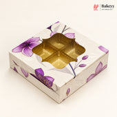 A square bakery gift box with a floral design featuring purple flowers and gray leaves on a cream background. The top has a decorative cutout window showing a gold-colored interior tray.