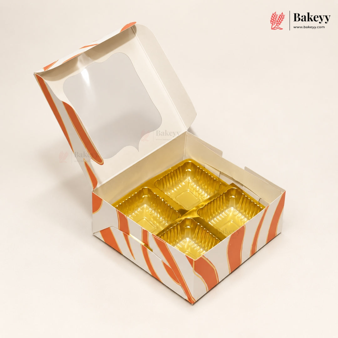 An open square bakery box with a clear window on the lid and orange-and-white wavy stripes, showing four gold foil compartments inside. The Bakeey logo appears in the top right corner.