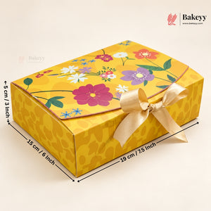 A yellow rectangular bakery gift box with a floral print on the lid and a cream ribbon bow, shown with dimension lines indicating measurements of 19 cm length, 15 cm width, and 5 cm height. The Bakeyy logo is visible in the top right corner.