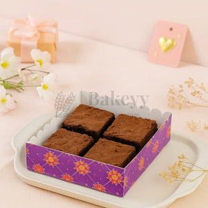 Four brownies in a decorative purple box on a white plate with flowers and candles in the background.
