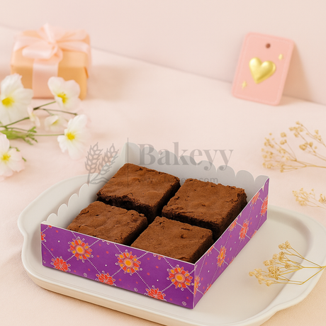 Four brownies in a decorative purple box on a white plate with flowers and candles in the background.