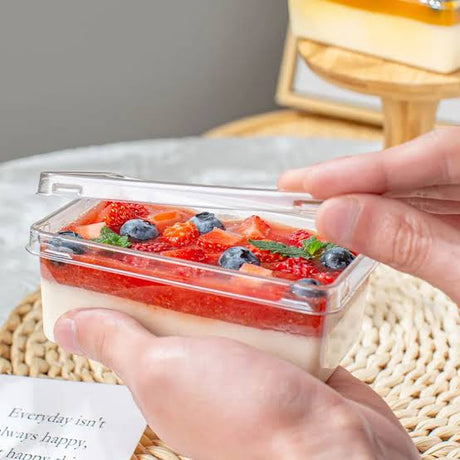 Hand holding a container of dessert with strawberries and blueberries on a textured surface.