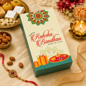 A rectangular gift box for Raksha Bandhan sits on a beige fabric surface surrounded by festive props, including almonds, a red and gold Rakhi, sweets, flowers, a lit lotus candle, and a gold ribbon. The box front is cream with a colorful mandala design, red script reading 'Happy Raksha Bandhan,' and illustrations of gift boxes and a diya.