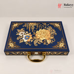 A rectangular navy blue decorative box with ornate gold floral and botanical embossed patterns on the lid, a gold handle, and gold trim along the edges, photographed on a light neutral background. Bakeyy branding is visible in the top-right corner.