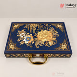 A rectangular navy blue decorative box with ornate gold floral and botanical embossed patterns on the lid, a gold handle, and gold trim along the edges, photographed on a light neutral background. Bakeyy branding is visible in the top-right corner.