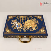 A rectangular navy blue decorative box with ornate gold floral and botanical embossed patterns on the lid, a gold handle, and gold trim along the edges, photographed on a light neutral background. Bakeyy branding is visible in the top-right corner.