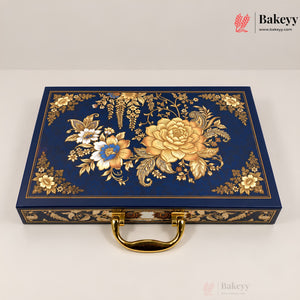 A rectangular navy blue decorative box with ornate gold floral and botanical embossed patterns on the lid, a gold handle, and gold trim along the edges, photographed on a light neutral background. Bakeyy branding is visible in the top-right corner.