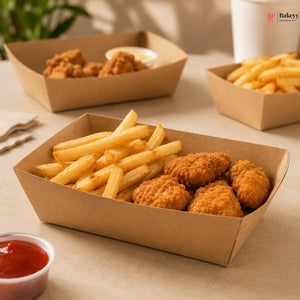 Cardboard containers with fried chicken and french fries on a table with a plant and cup in the background.