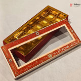 An ornate rectangular gift box with a red and gold floral-patterned lid and a gold foil-lined interior, shown open on a light gray background. A Bakeey logo appears in the top right corner.