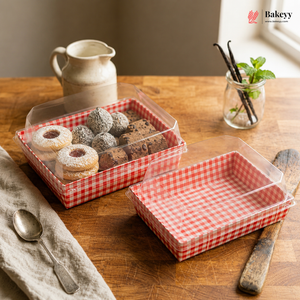 Clear plastic containers with red checkered lining on a wooden table, containing small pastries, with 'Bakey' branding.