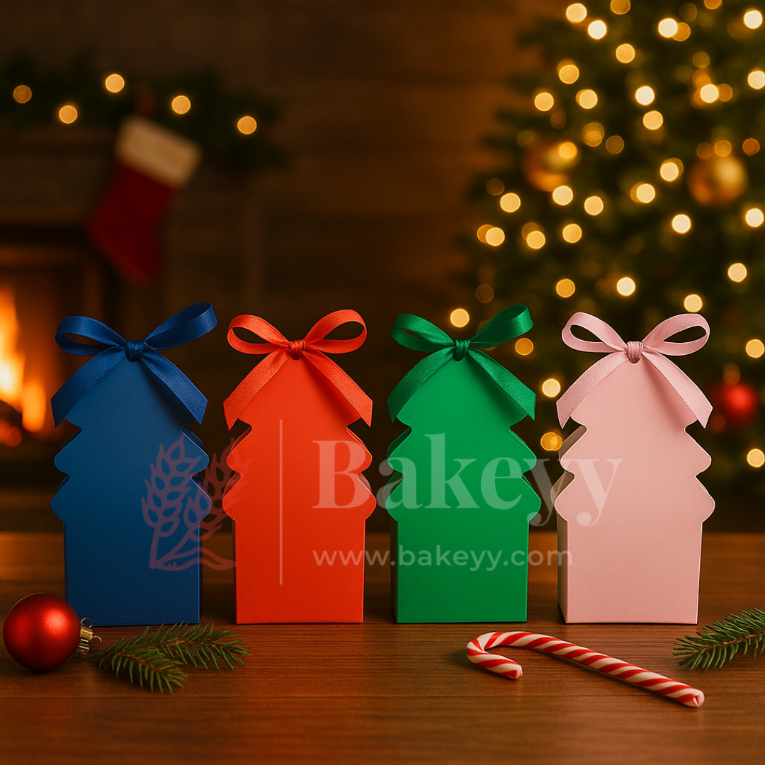 Four colorful Christmas tree-shaped boxes with ribbons on a wooden table, decorated with a Christmas tree and candy cane in the background.