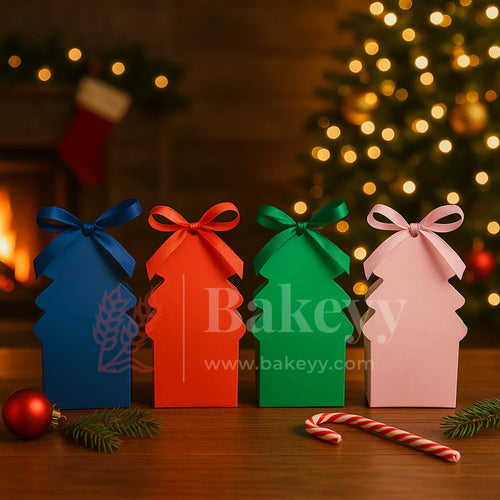 Four colorful Christmas tree-shaped boxes with ribbons on a wooden table, decorated with a Christmas tree and candy cane in the background.