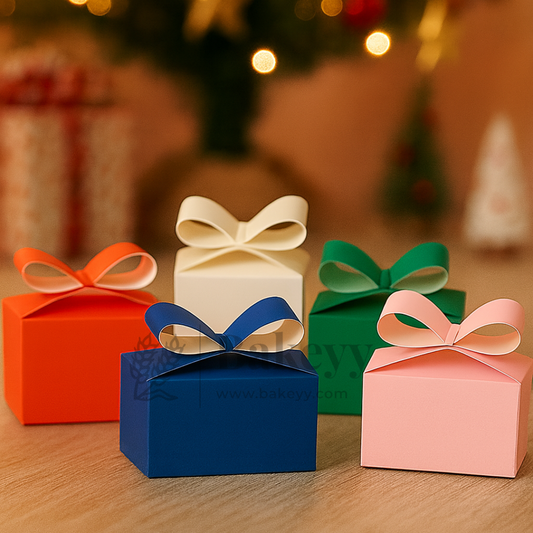 Four colorful gift boxes with ribbons on a wooden surface, blurred Christmas tree in the background