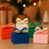 Four colorful gift boxes with ribbons on a wooden surface, blurred Christmas tree in the background