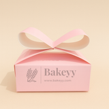 Pink gift box with a ribbon on a beige background, featuring the brand 'Bakeyy'.