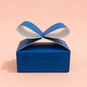 Blue box with a blue ribbon on a pink background, featuring the brand 'Bakeyy'.