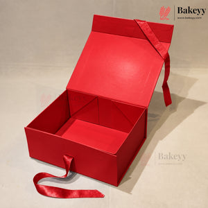 An open red bakery gift box with a matching red satin ribbon handle, photographed on a light beige studio background. The Bakeey brand logo is visible in the top right corner.