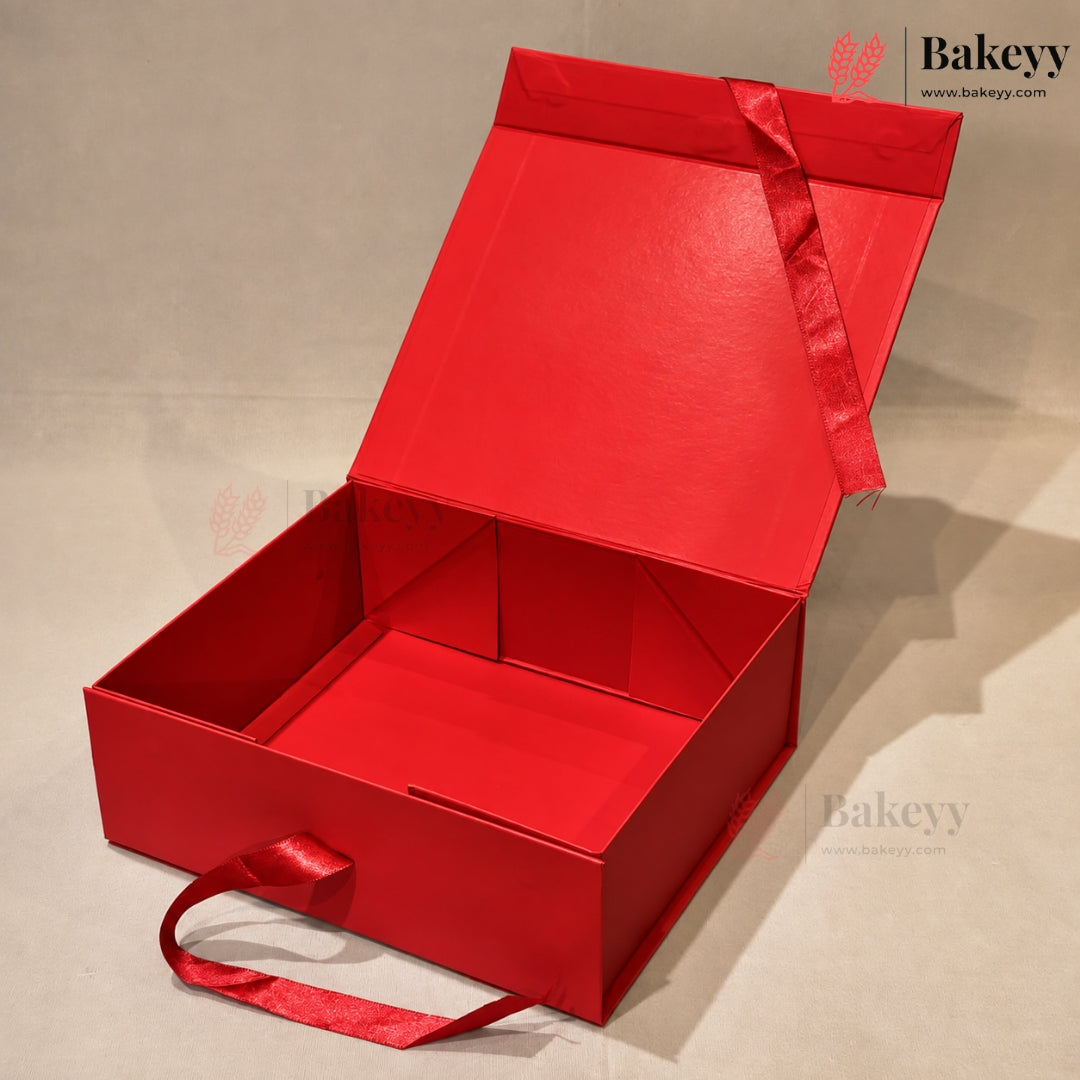 An open red gift box with a matching red ribbon handle, photographed on a neutral light gray background. The brand name Bakeyy is visible as a watermark in the top right and on the bottom right.