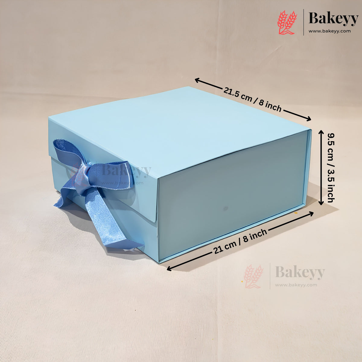 A light blue rectangular gift box with a matching blue ribbon bow on the side, shown on a beige background with dimension arrows and text indicating 21.5 cm by 9.
