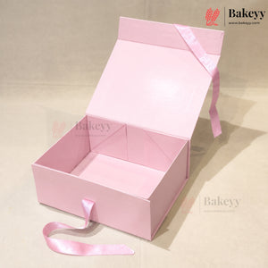 An open light pink cardboard gift box with a matching pink satin ribbon tied around the lid, photographed on a plain beige background. The brand name Bakeey is visible as a watermark and logo in the top right corner.