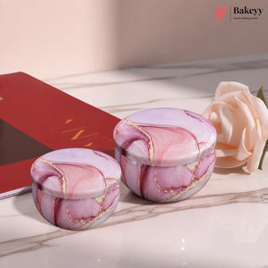 Two round pink marble-patterned lidded containers with gold veining, displayed on a marble surface next to a red book and a pale peach rose. A Bakeey logo watermark is visible in the top right corner.
