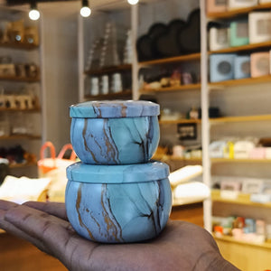 Two stacked round blue marble-patterned jars held in a person's hand inside a softly blurred retail store setting.