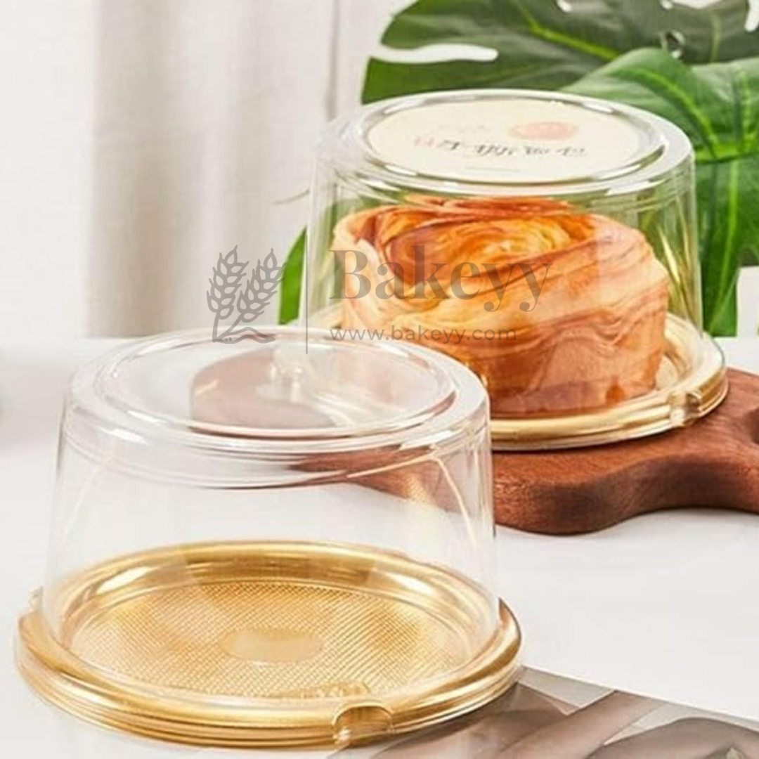 Clear cake stand with gold base on a white surface with green leaves in the background