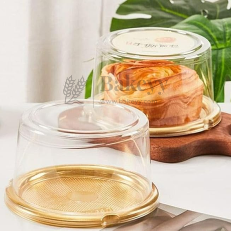 Clear cake stand with gold base on a white surface with green leaves in the background