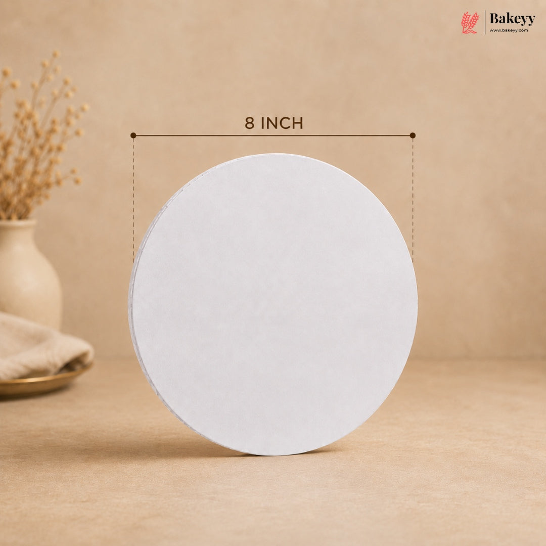 An 8-inch round white cake or cookie cutter standing upright on a beige surface, with a dimension line labeled '8 INCH' above it. The background is a warm beige studio setting with a vase and dried flowers at left, and a Bakeey logo in the top right.