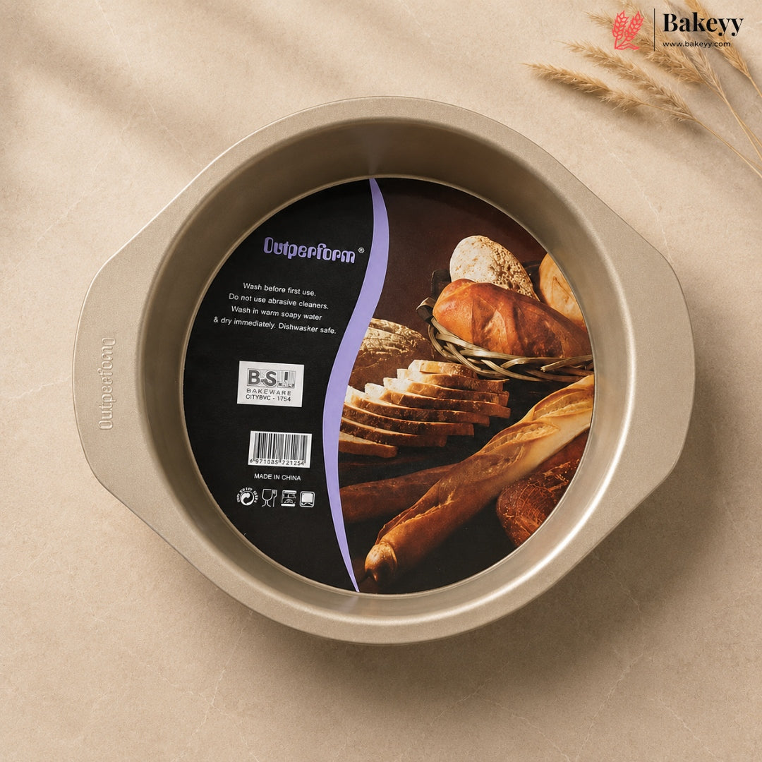 A round non-stick baking pan with side handles, shown from above on a beige fabric background with wheat stalks. The inside has a black and purple product label featuring bread imagery and the brand name 'Outperform'.